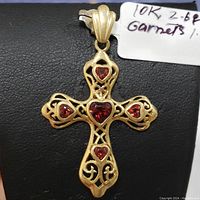 Front angle of the gold cross pendant showing intricate filigree and garnet stones.
