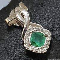 Close-up image of 10K white gold pendant featuring a central cushion-cut green emerald surrounded by small white stones in a halo setting, with a flowing white gold bale.