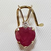 Close-up front view of the heart-shaped ruby pendant with diamond accent, showing the gold prongs and clasp mechanism.