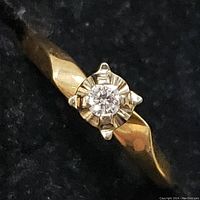 Close-up of diamond and starburst-style prong setting on yellow gold band.