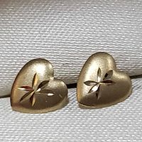 Close-up front view of a pair of heart-shaped yellow gold stud earrings with star-shaped engraving on each earring.