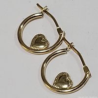Top-down view of pair of 14K gold hoop earrings with heart charms.