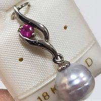 Close-up view of the 18K white gold pendant showing the ruby and South Sea pearl with the 18K gold label visible.