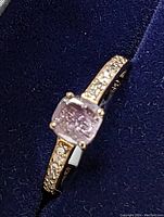 Angled view of the ring centered on the cushion cut pink diamond showing the yellow gold band and pavé diamonds