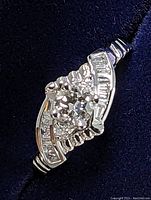 Front view of ring showing central round and side diamonds on dark fabric