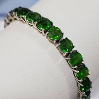 Close-up of multiple green tourmaline gemstones set in sterling silver prongs on a white display cuff