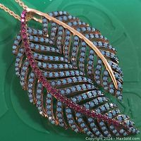 Close-up of leaf-shaped pendant showing rose gold plating with purple stones along central vein and light blue stones on leaf body.