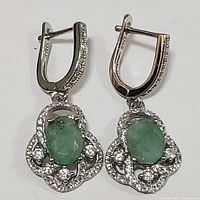 Front view of sterling silver earrings showing oval green emerald stones surrounded by cubic zirconia