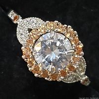 Close-up image of the sterling silver ring showing the round moissanite center stone with surrounding champagne-colored stones and white stone accents on black background.