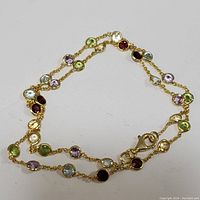 Full view of gold-tone sterling silver necklace with multiple bezel-set round faceted gemstones in various colors.