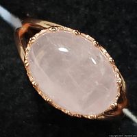 Close-up of oval rose quartz cabochon set in sterling silver ring with decorative bezel.