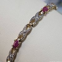 Close-up showing the interlinked sterling silver segments with small clear stones and oval red ruby gemstone.