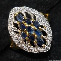 Close-up photo of an elongated oval sterling silver ring with marquise sapphires and white accent stones on a black background.