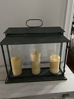 Front view of the rectangular 3-candle lantern with heavy glass and dark metal frame, showing the three candles inside.