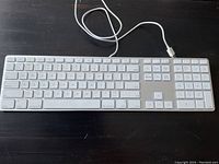 Top view of Apple wired keyboard showing full key layout, white keys and aluminum base, connected with a USB cable