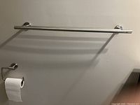 Toilet tissue holder matching the towel bar, mounted on wall with roll of toilet paper.