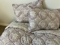 Photo showing the boho style reversible quilt laid out with two matching pillow shams placed at the head of the bed, clear view of the medallion pattern and one reverse corner flipped to show geometric pattern.
