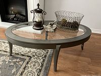 Full view of the oval coffee table with glass top insert and decorative items arranged on top, highlighting the table's shape, glass surface, soft metallic finish, and positioning of decor pieces.