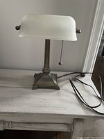 Front view of the desk lamp showing the white textured glass shade and the ornamented metal base with power cord visible.