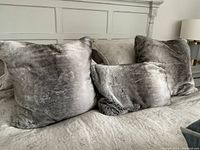 Three luxurious faux fur pillows on a bed: two square ones (20 inches) and one rectangular (22x14 inches) in silvery gray color.