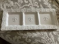 Top view of the white ceramic divided tray with three square sections and decorative embossed edges with fleur-de-lis symbols in the center of each section.