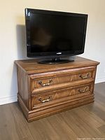 Insignia flat-screen TV placed on a wooden cabinet showing the front view. TV is black and includes remote.