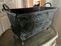 Side view of the rectangular metal planter showing ornate scroll patterns, handles, and legs.