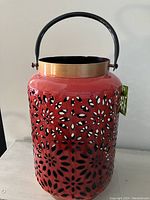 Front view of red metal lantern showing floral cutouts and handle with attached tag.