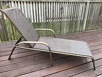Beige fabric mesh lounge chair with metal frame on wooden deck.