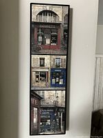Full frontal view of the wooden wall art showing all three Paris storefront paintings vertically arranged with black frame.