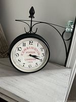 Front side clock face showing 'Kensington Station London 1879',' time 3:20, black metal frame with wall mounting arm.