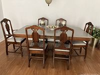 Front view of wooden dining table with painted tabletop surrounded by six chairs, one with arms.