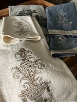 Four towels arranged on a wooden tray showing embroidery details on blue, cream, and gray towels.