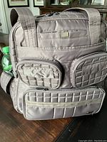 Front angled view showing multiple zippered compartments, quilted nylon material, Lug logo tag, and bottle pocket on side