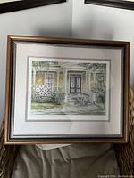 Framed limited edition print showing a porch scene with a quilt and a person working, signed and titled by artist Trisha Romance.