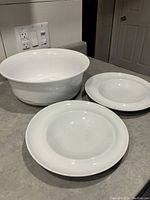 Set of white ceramic serving dishes and plates with different sizes visible on kitchen counter.
