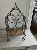 Front view of metal and wicker wine holder rack showing circular bottle holders and wicker base