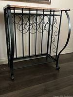 Full view of metal wine rack with wood top on dark floor, showing curved side detail and circular bottle holders front.