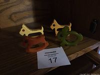 Four Bakelite napkin rings shaped as two Scotty dogs, a rabbit, and a rocking horse on a wooden shelf with a maxsold lot card.