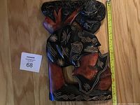 Single wooden carving depicting a woman's face in profile with a tree above her head on a flat background. The carving has detailed black and white painted patterns on the hair and tree.