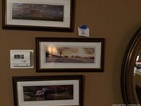 Three framed panoramic photos hung on wall above thermostat and mirror. Mill and barn fall scenes.