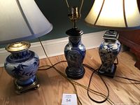 Photo of three blue and white ceramic table lamps with two having fabric shades, showing varied shapes and bases, cords visible