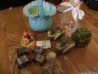 View of all items together showing blue ceramic basket, wooden rabbit containers with eggs, metal napkin rings, humming figurine, artichoke candle, glass rose vase, and soft duck basket
