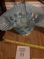 Front angle showing the light blue basket with fluted edge, circular cutout pattern, and clear glass handle