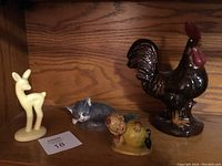 Full view of all four figurines including the fawn, sleeping cat, lemon boy, and rooster on a wood surface.