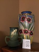 Two urn vases and pewter jug displayed on wooden furniture against a beige wall.
