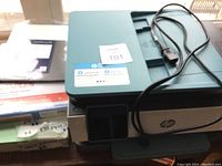 HP OfficeJet Pro 8028 printer on desk with power cable and paper packs visible