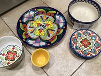 Photo showing colorful large plate, bowls, bread and butter plates, and small yellow bowl arranged on floor.