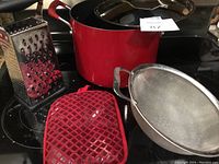 Photo showing the red Kitchen Aid 8 quart pot, metal cheese grater, red oven mitt and metal strainer on stovetop