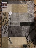 Overall view of the area rug showing geometric and botanical patchwork design in grey, tan, black, and taupe colors.